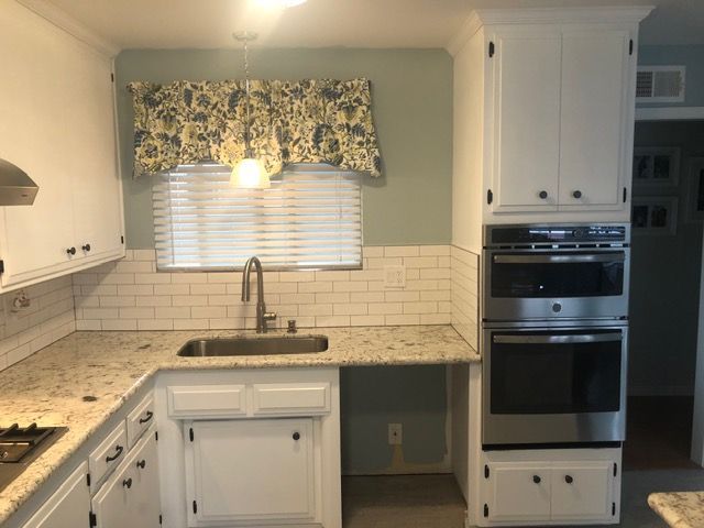 Bright kitchen with white cabinets, tiled backsplash, window over sink, and built-in oven.
