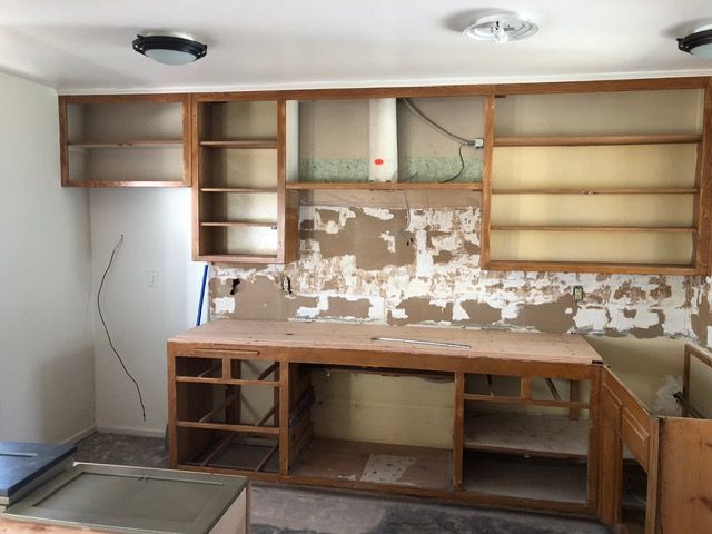 Partially demolished kitchen with exposed cabinets, bare wall, and damaged countertop