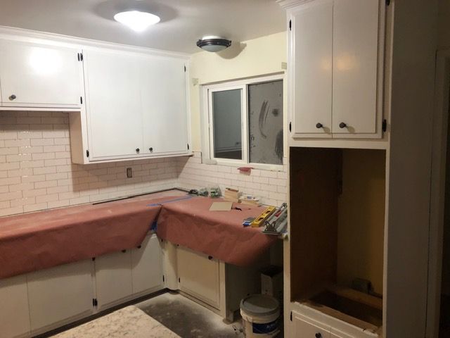 Kitchen under renovation with red countertops, white cabinets, and an unfinished corner cabinet opening