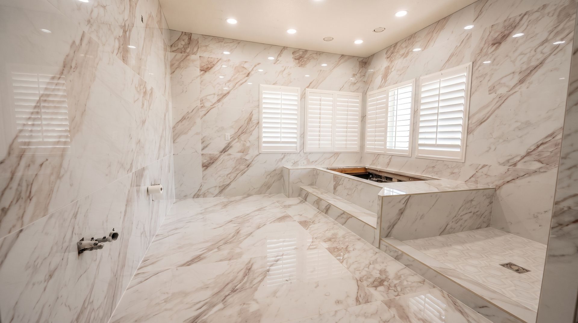Marble bathroom with glass-enclosed tub, shower fixtures, and mosaic tile floor