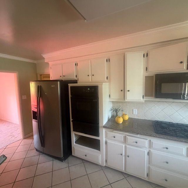 Bright kitchen with white cabinets, stainless steel fridge, built-in oven, and tiled floor.