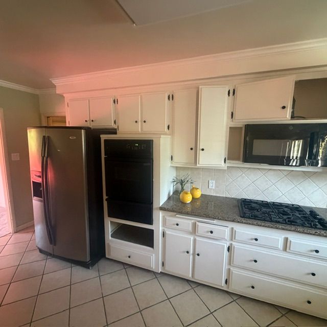 Bright kitchen with white cabinets, stainless fridge, black oven, and tiled floor