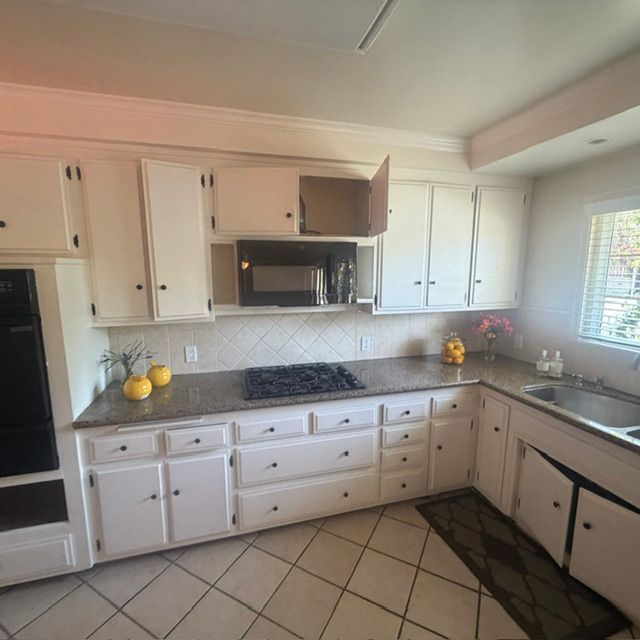 Bright white kitchen with tiled floor, black appliances, white cabinets, and fruit on the counter