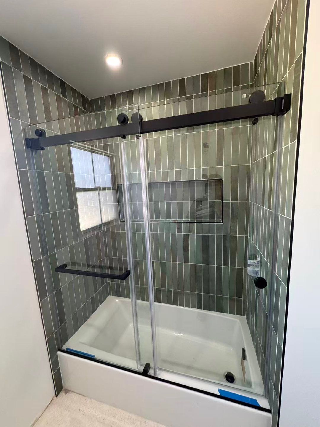 Glass-enclosed shower stall with striped tile walls and a white tub base