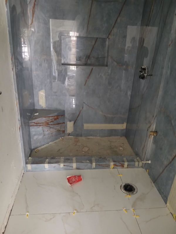Tiled bathroom shower under construction with gray walls, white floor, and exposed drain and fixtures
