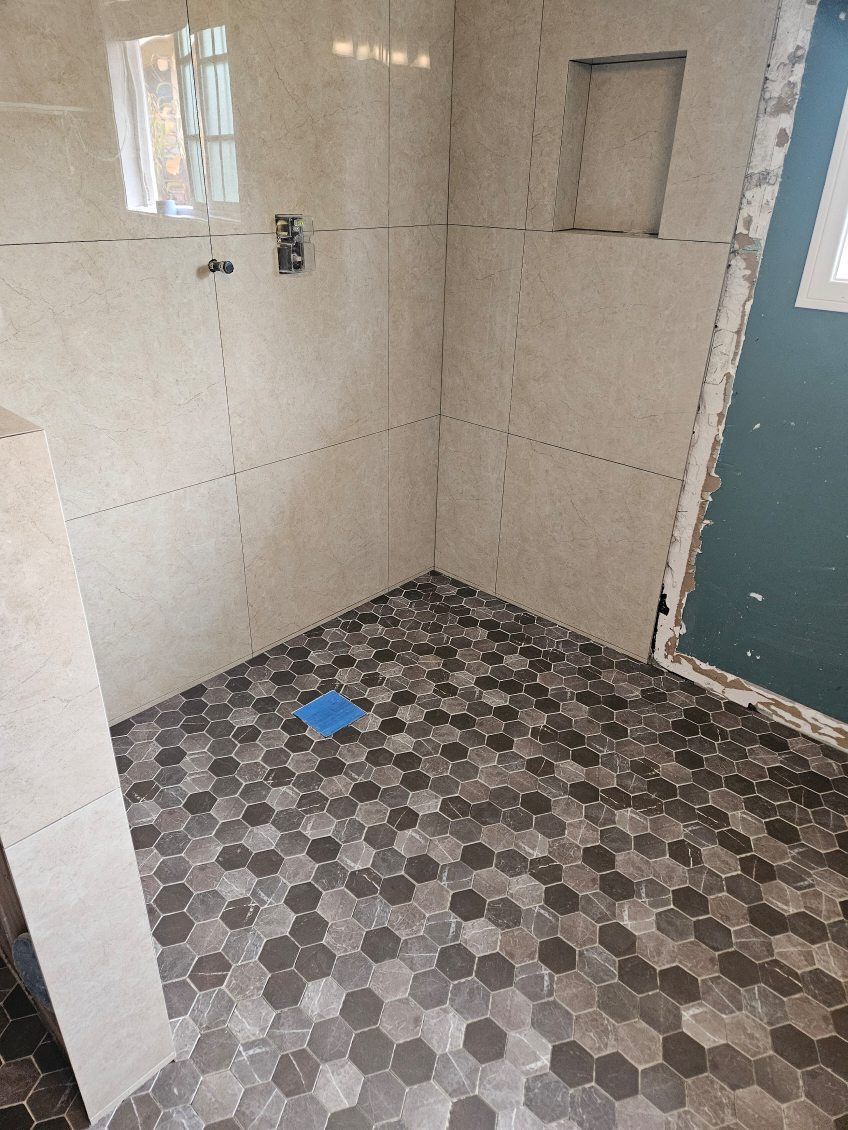 Small tiled bathroom with beige walls, patterned floor, a shower stall, and a blue mat on the floor.