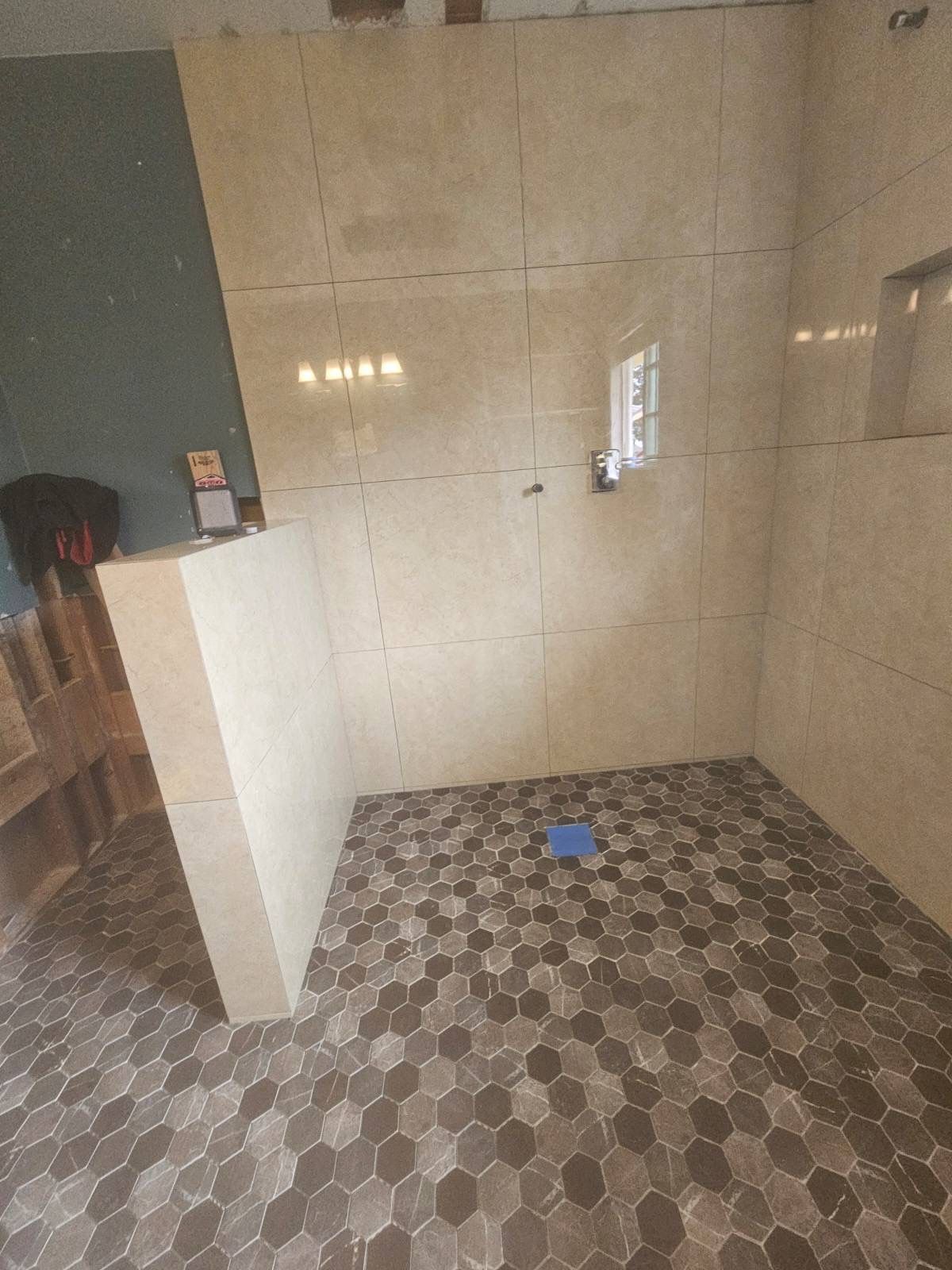 Tiled bathroom/shower area with beige walls, patterned floor, and a blue floor drain cover