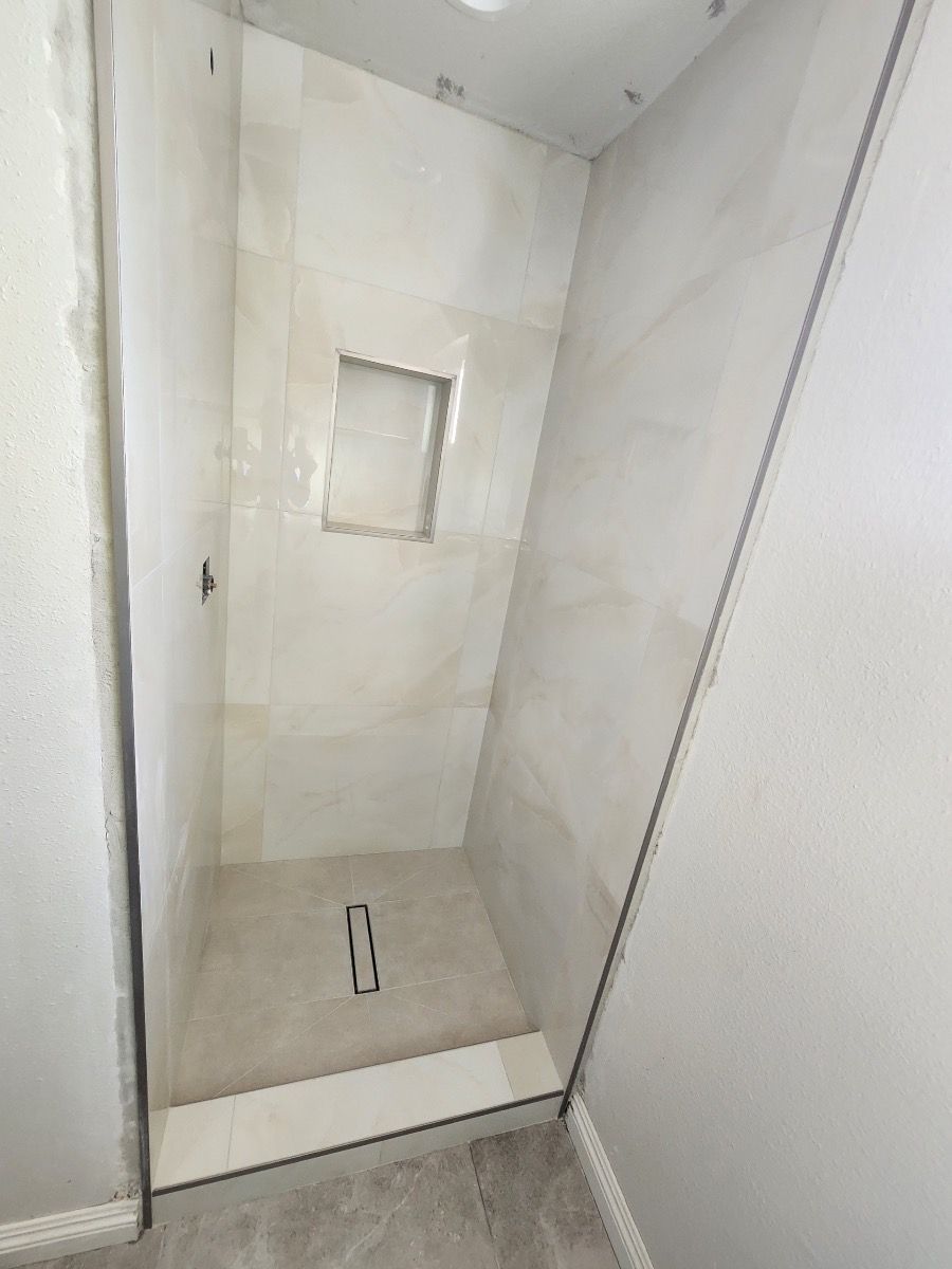 Empty white shower stall with a small recessed window and drain