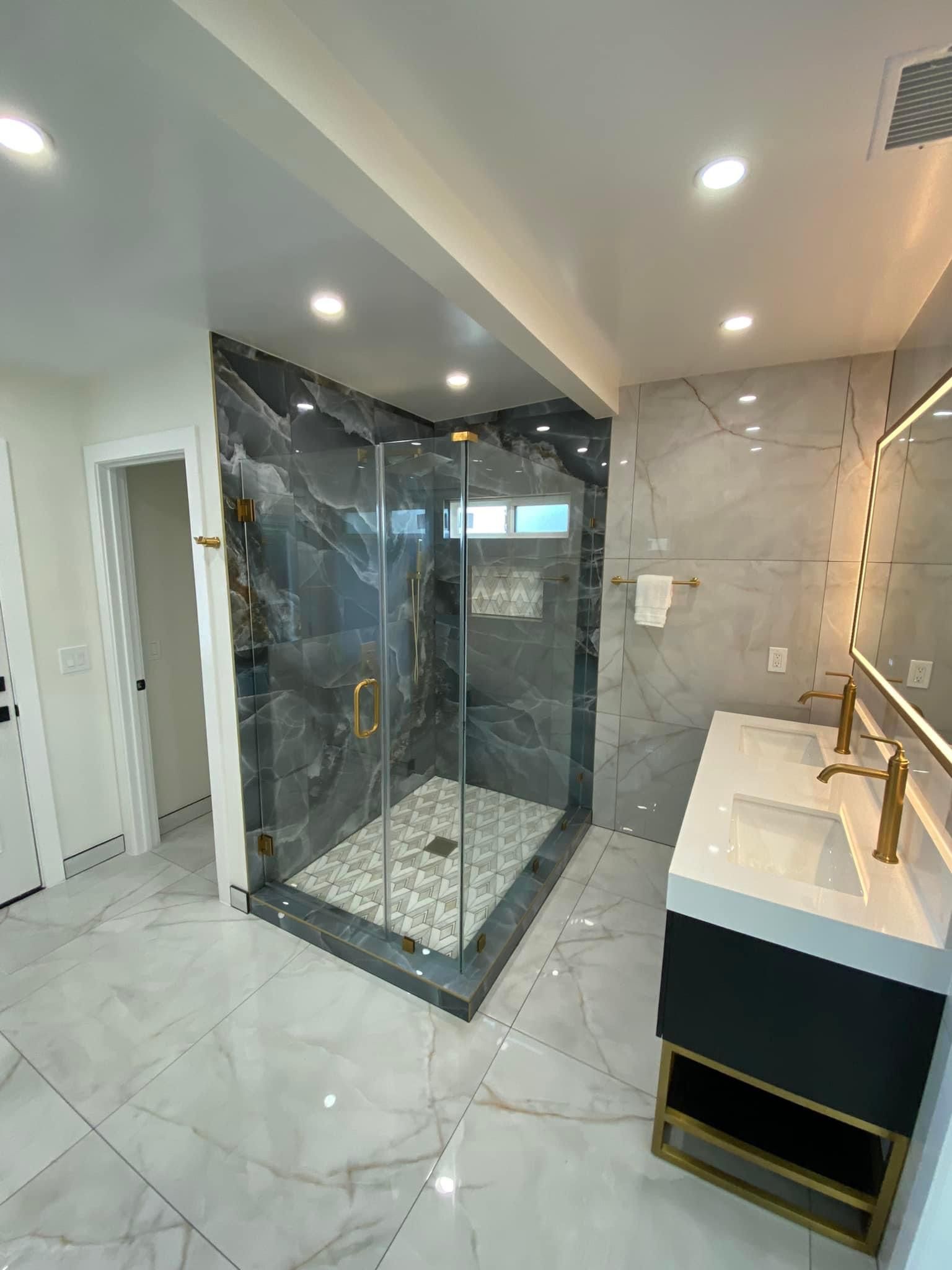 Modern bathroom with glass shower, marble tile, and white vanity with gold faucet