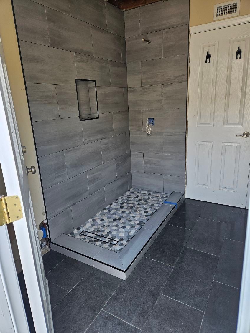 Small tiled shower area with gray walls, pebble shower floor, and a white door beside it