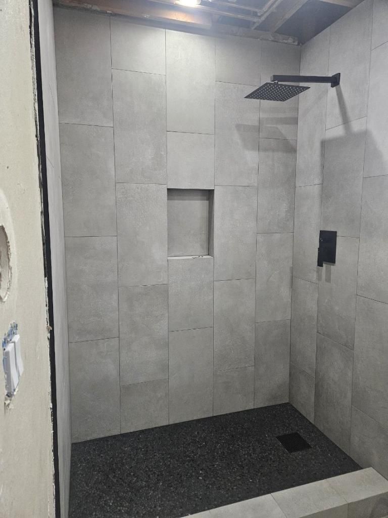 Tiled shower stall with black shower pan, wall niche, and overhead showerhead.