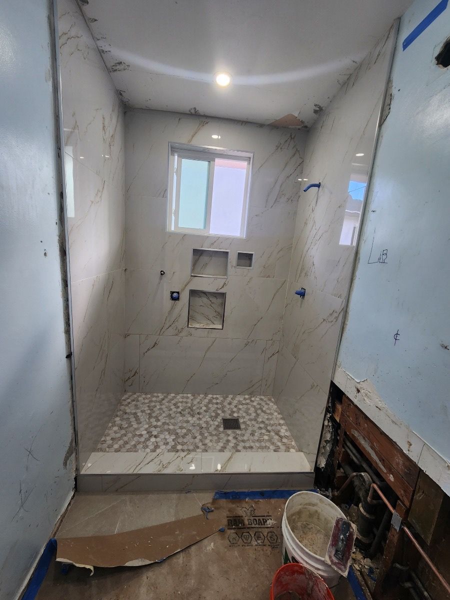 Narrow unfinished bathroom under renovation, with tiled floor, window, and exposed plumbing.