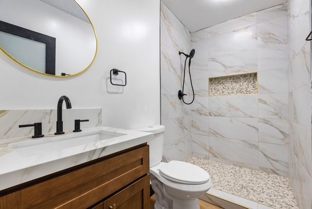 Modern bathroom with white marble shower, black fixtures, wood vanity, and round mirror