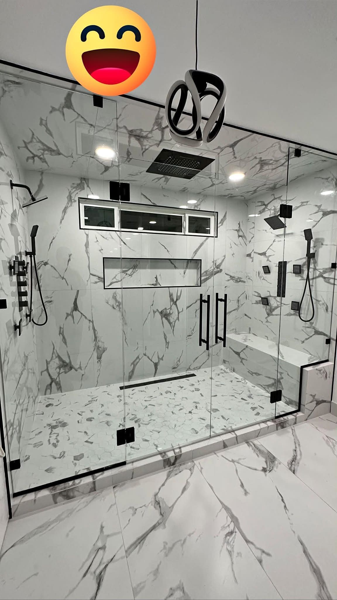 Modern marble-tiled bathroom with glass shower enclosure, vanity, and bright ceiling lights.
