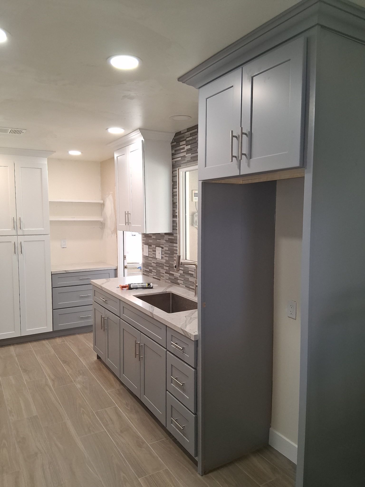 Narrow kitchen with white cabinets, gray island, recessed lights, and built-in washer-dryer nook.