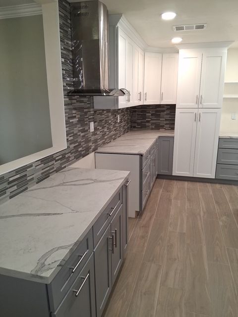 Modern kitchen with white cabinets, gray marble counters, mosaic backsplash, and wood-look flooring.
