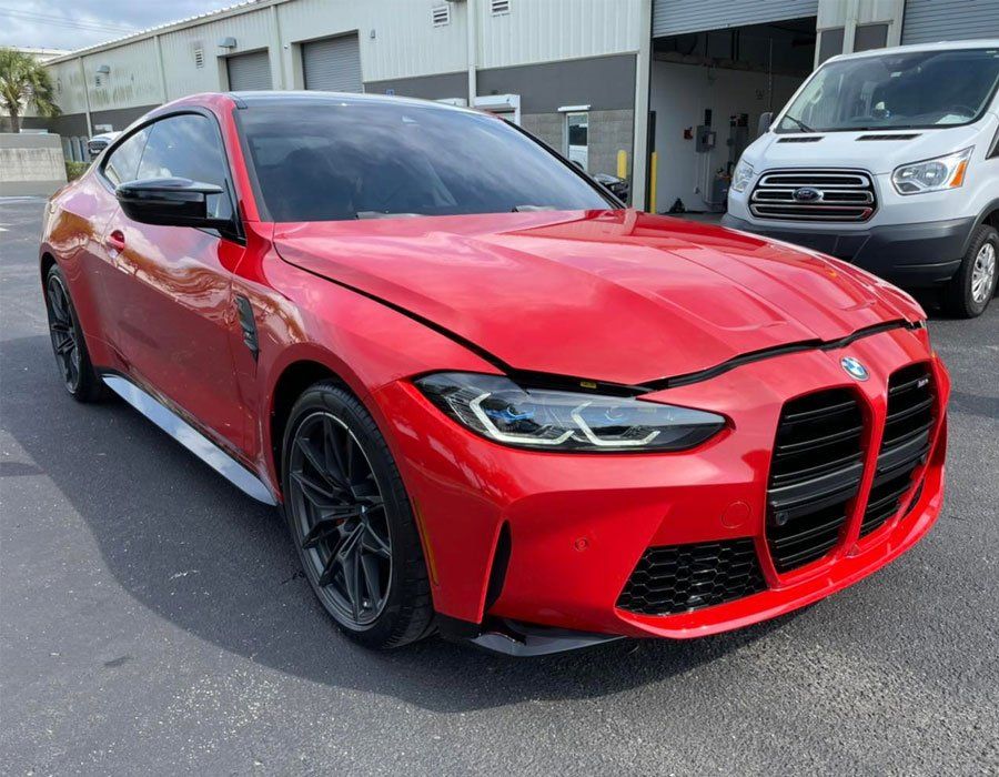 Red BMW M4 coupe with black accents parked outdoors near a van.