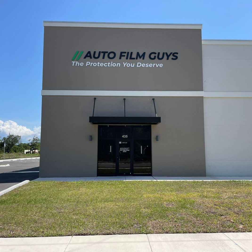 Exterior of Auto Film Guys store with green logo and black awning.