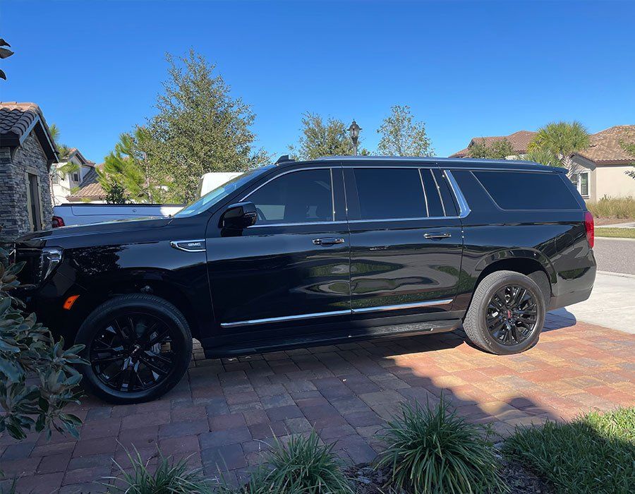 Black SUV parked on a brick driveway in front of a house on a sunny day.