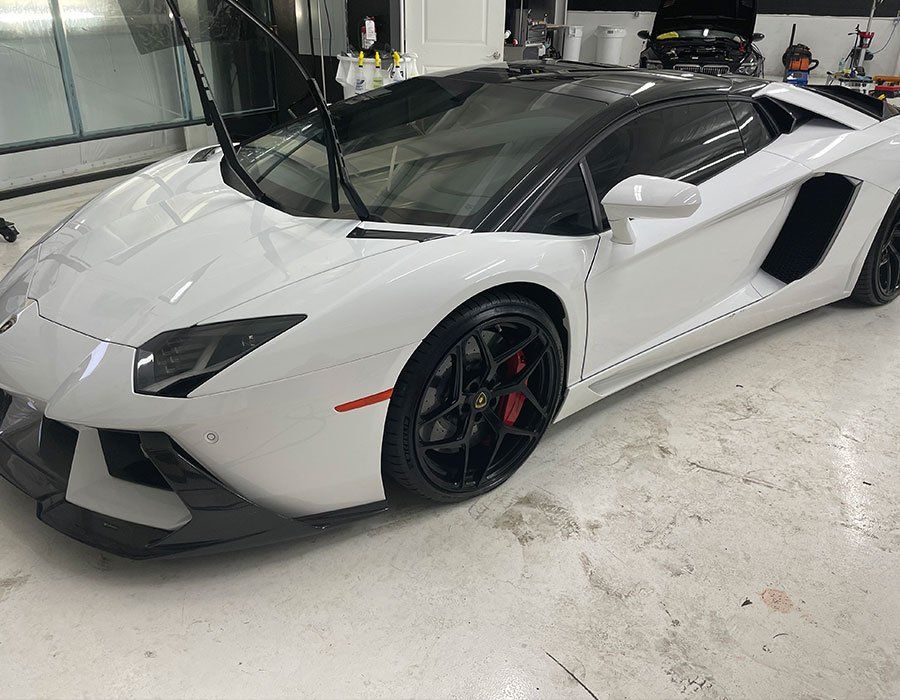 White Lamborghini sports car with black roof and wheels, parked in a garage.