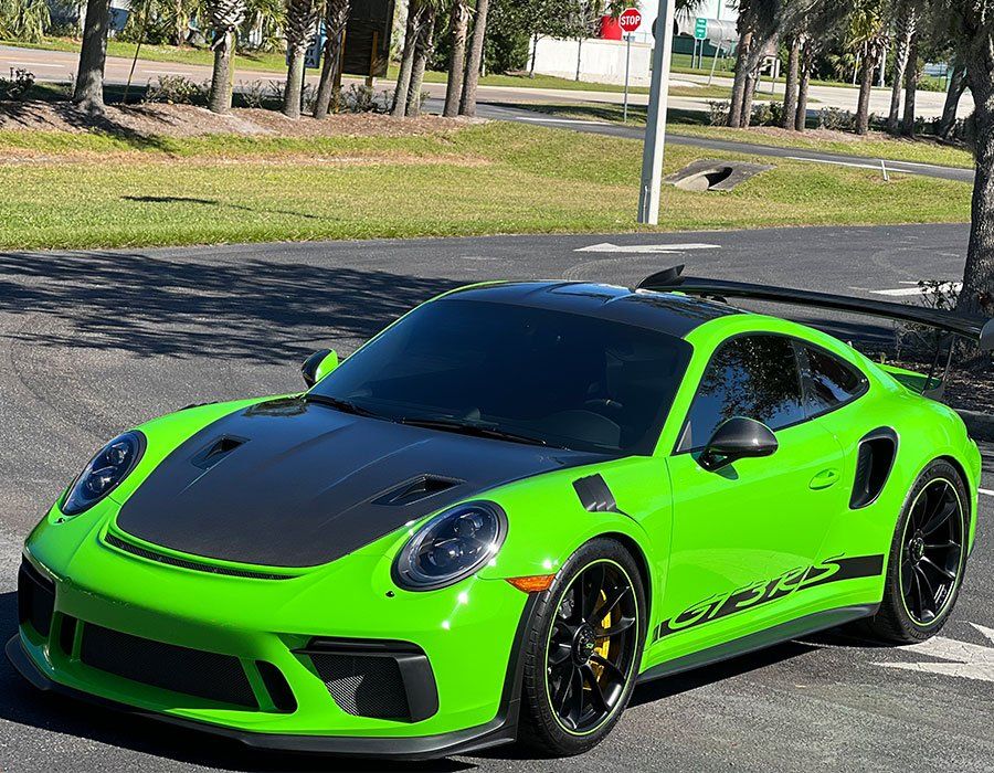 Bright green Porsche 911 GT3 RS parked on asphalt, with a black hood and spoiler.