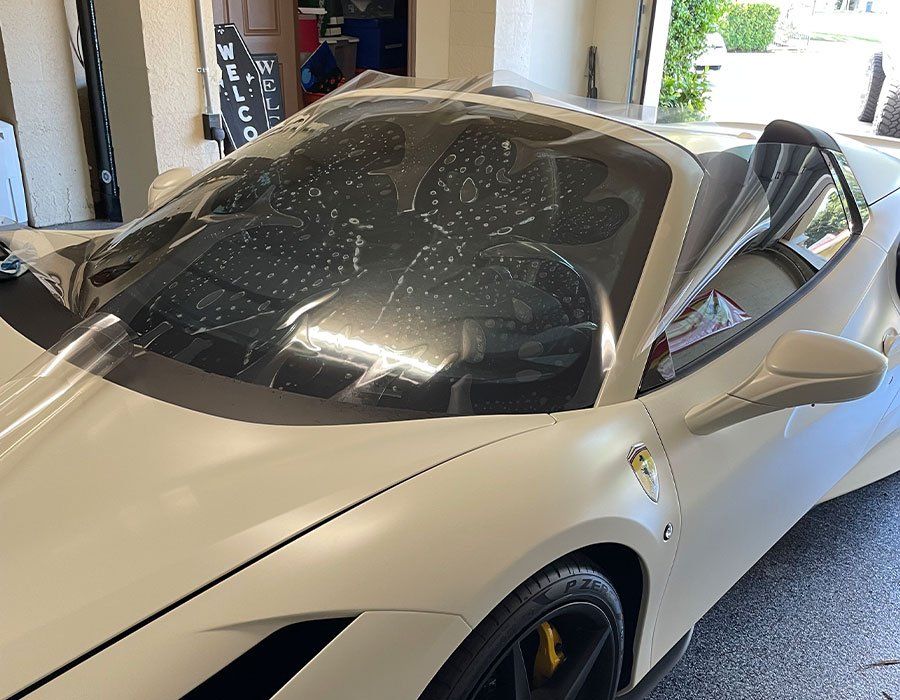 White sports car with window tint being applied in a garage.