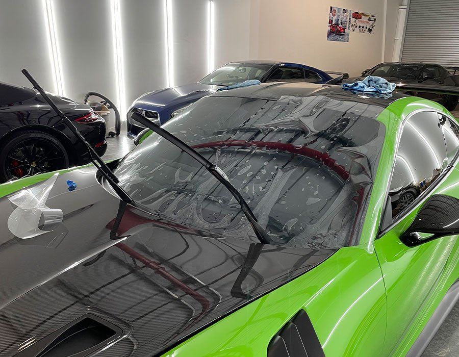 Green sports car with window film application in a garage setting.