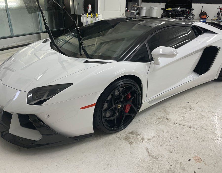 White Lamborghini sports car parked in a garage, black roof, red brake calipers.
