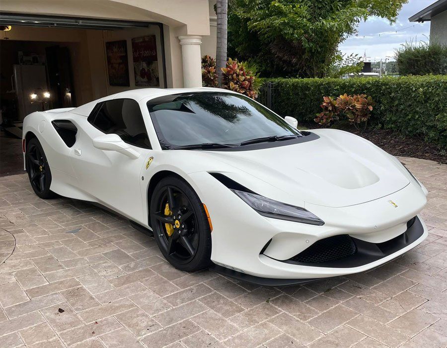 White Ferrari sports car parked in a driveway with a garage entrance in the background.
