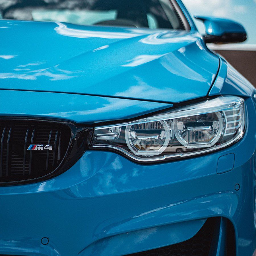 Blue BMW M4, close-up of the front, headlights, grille with M4 logo, parked outdoors.