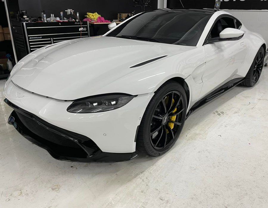 White Aston Martin sports car with black trim and yellow brake calipers parked inside a garage.