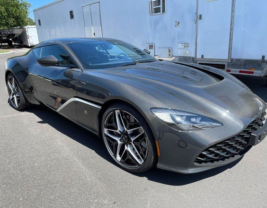 Dark gray Aston Martin sports car parked in front of a white trailer.