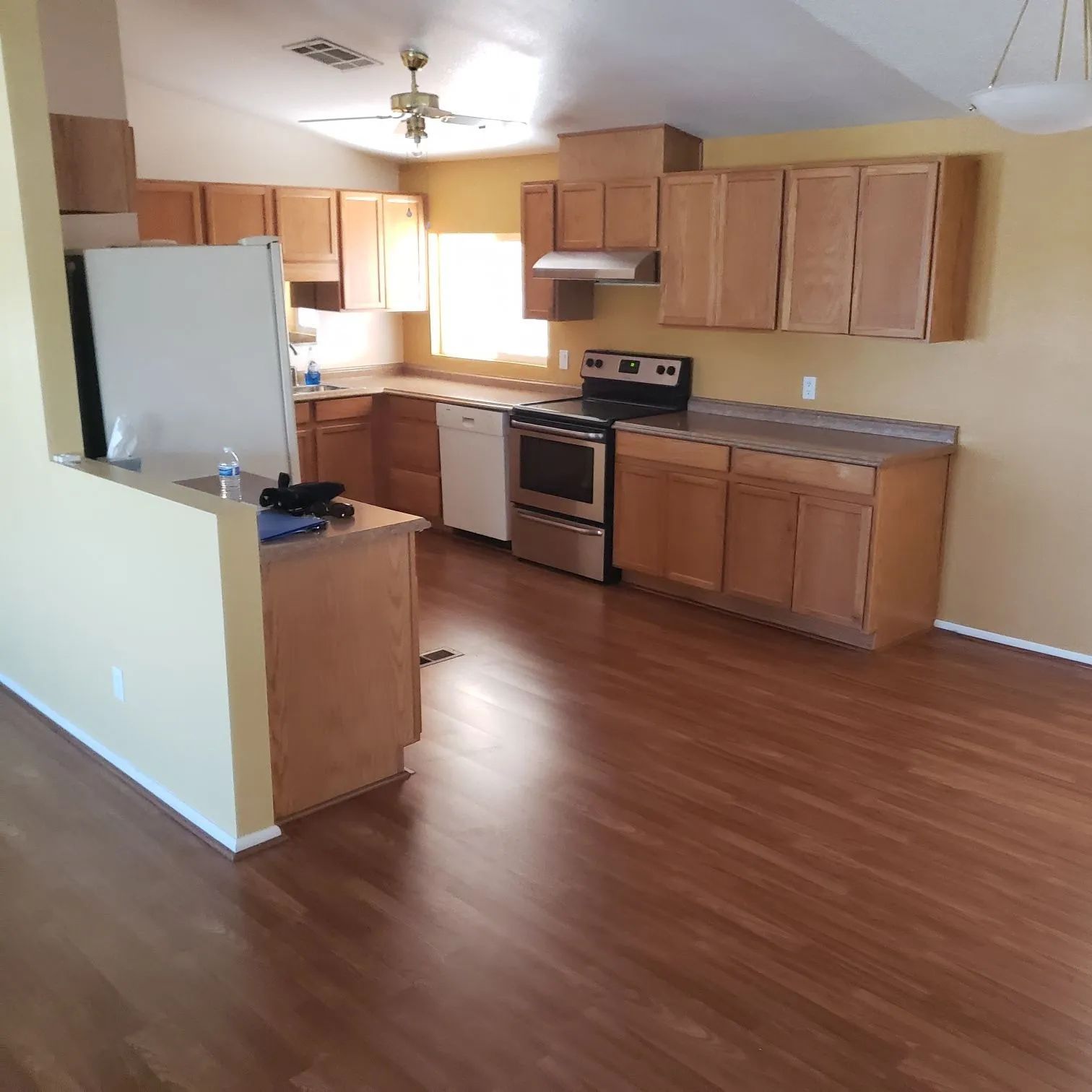 Empty kitchen and living area with wood cabinets, stainless stove, white fridge, and wood-look floors