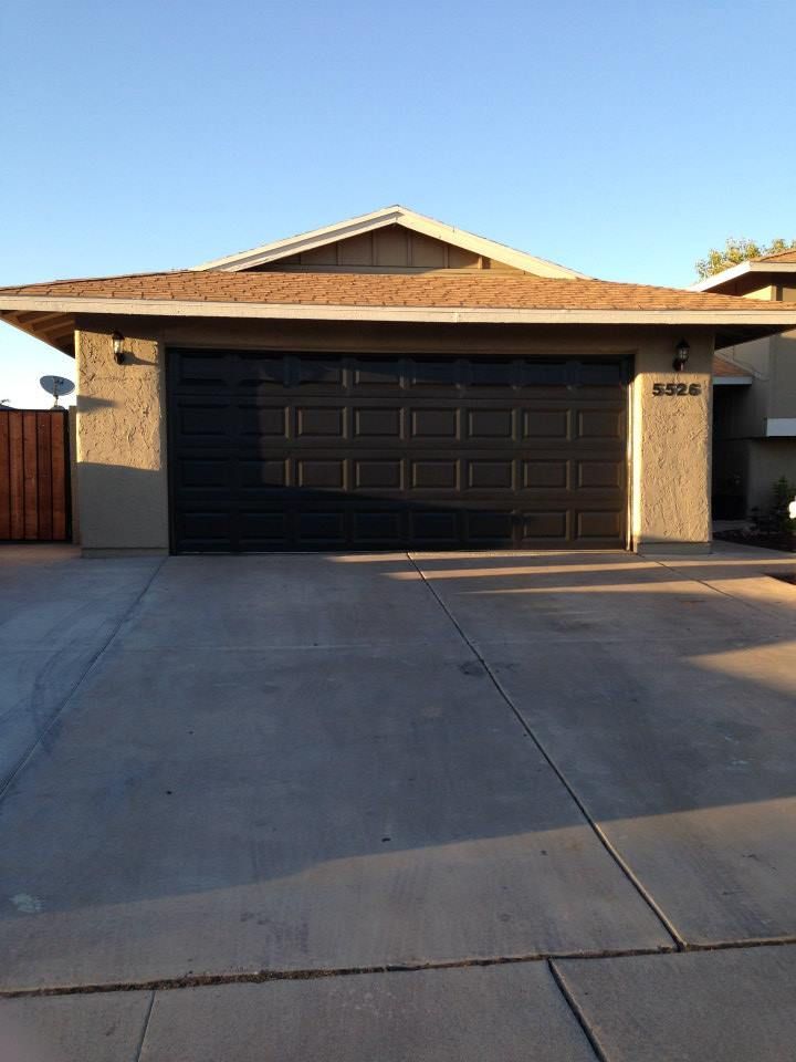 Gray house with black garage door and concrete driveway.