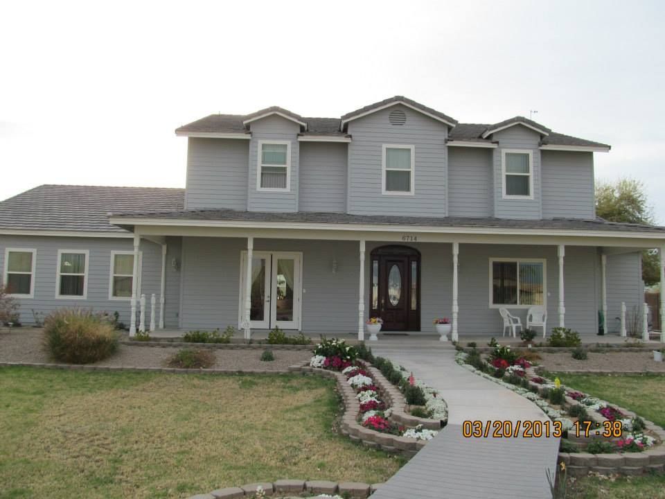 Two-story gray house with a porch, pathway lined with flowers, and a lawn in front.