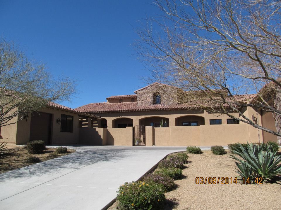 Tan stucco home with a red tile roof on a sunny day. Concrete driveway leads to the entrance.