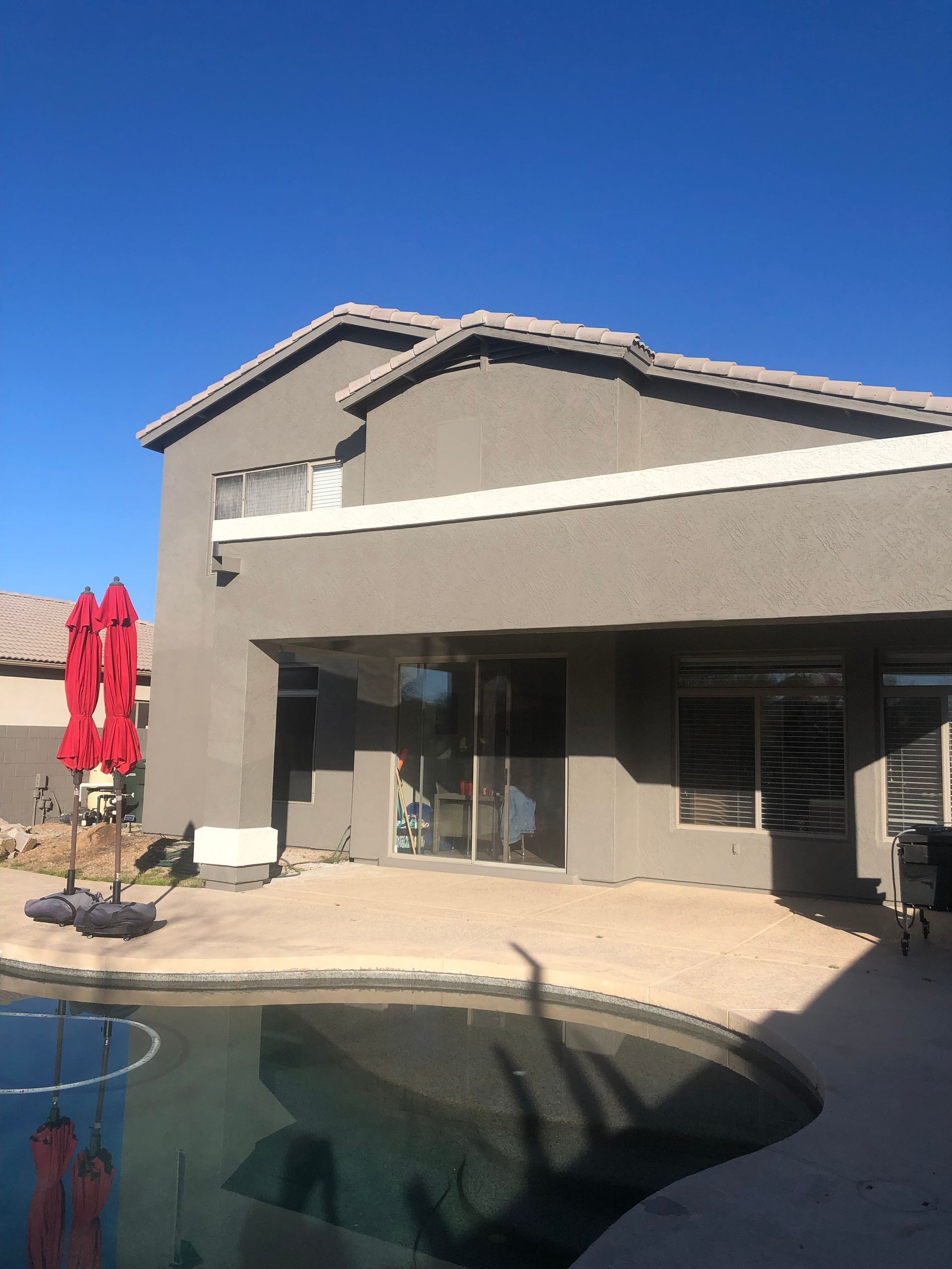 A two-story house with a gray exterior and a pool. A red umbrella provides shade.
