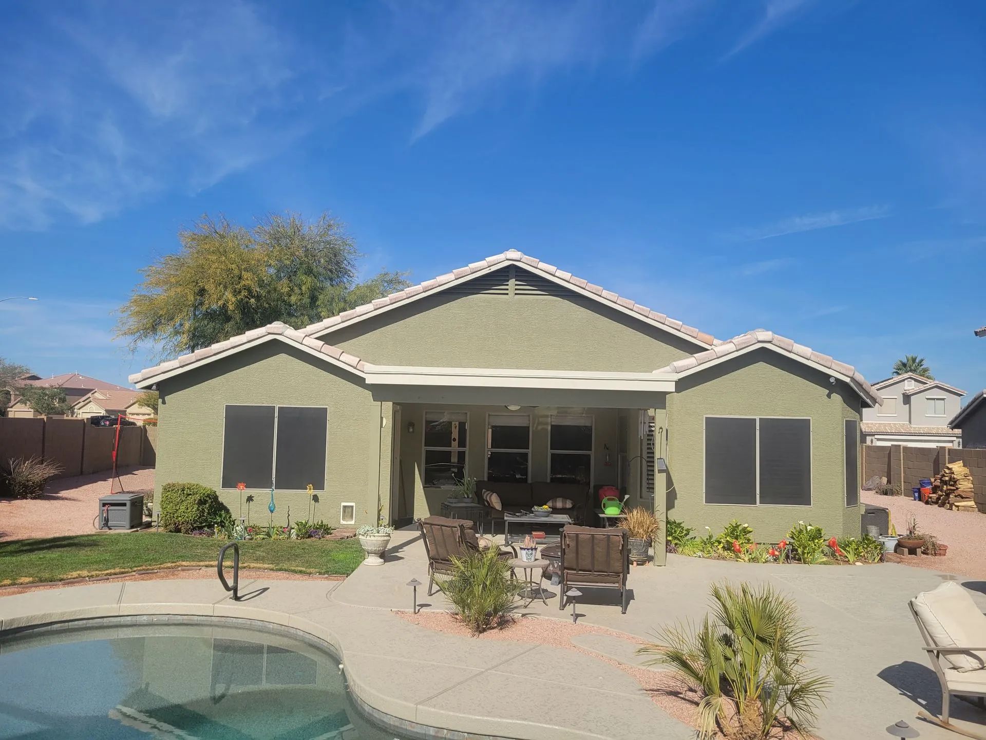 Single-story beige house with a covered patio, pool, and desert landscaping under a blue sky