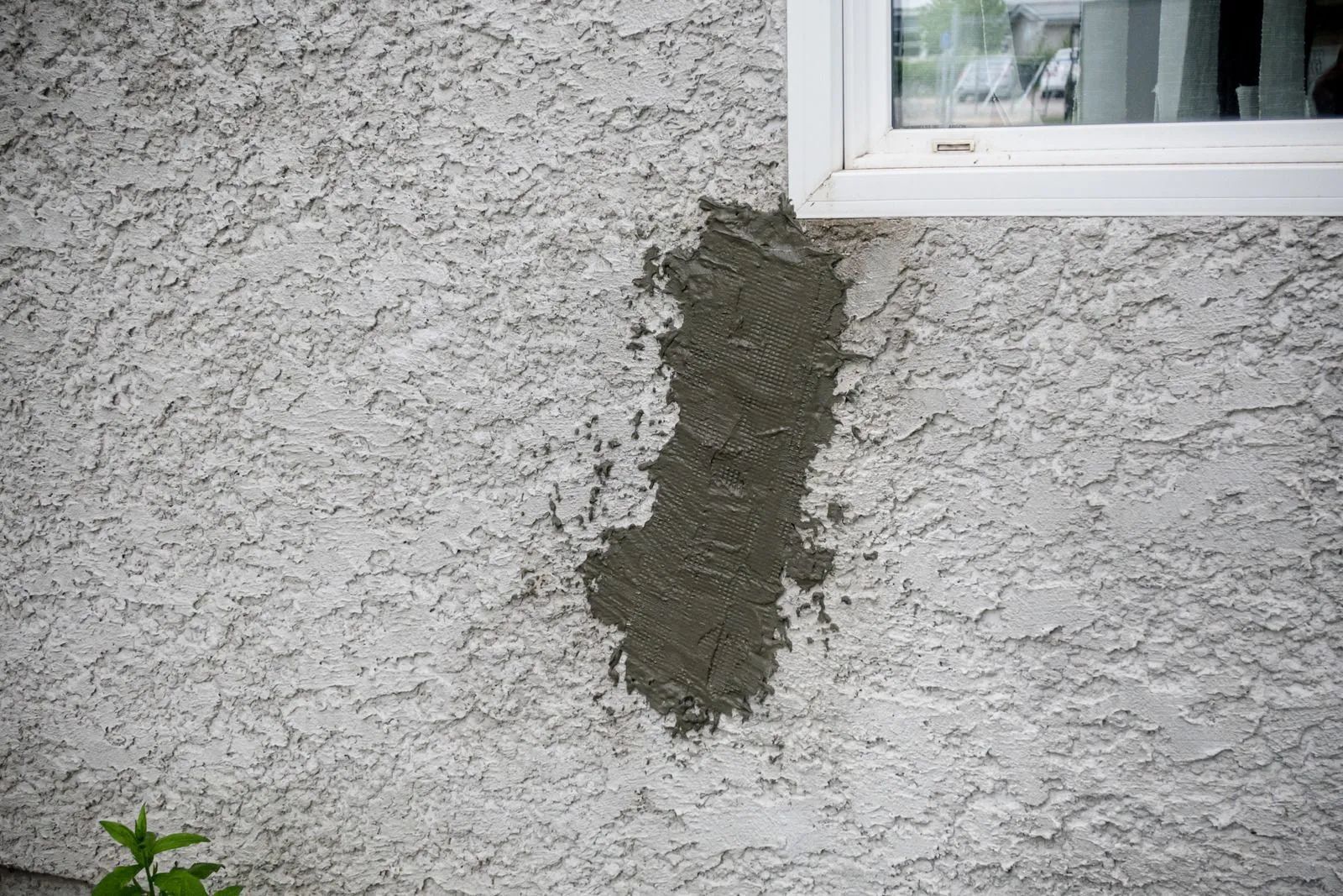 Fresh gray plaster patch on a textured stucco wall below a white window