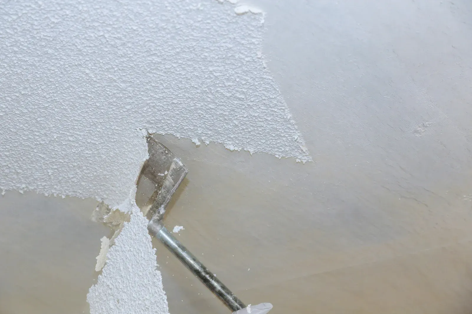 Paint roller applying white paint to a textured ceiling, covering a patch of old paint.