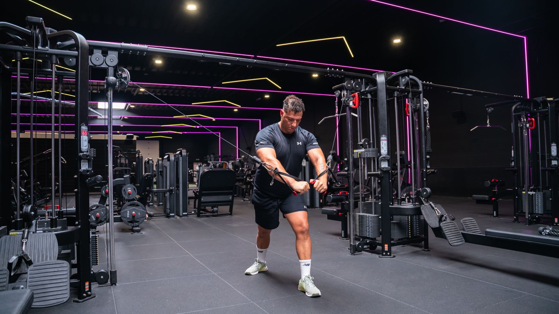 Een man traint zijn borstspieren met een kabelmachine in een sportschool. Zwarte en neonlichten op de achtergrond.