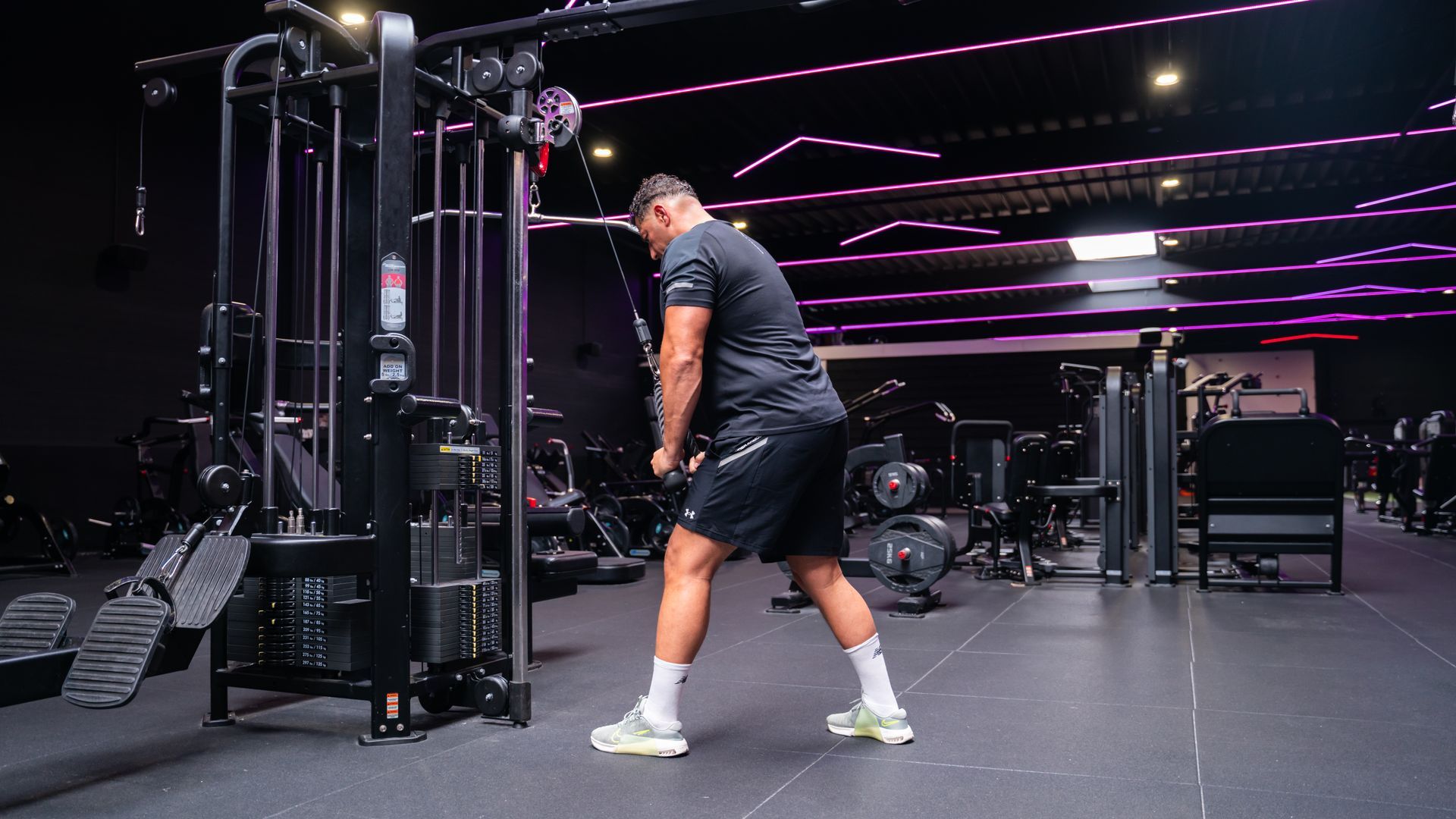 Een persoon in de sportschool gebruikt een kabelmachine, met gestrekte armen, en doet triceps pushdowns.