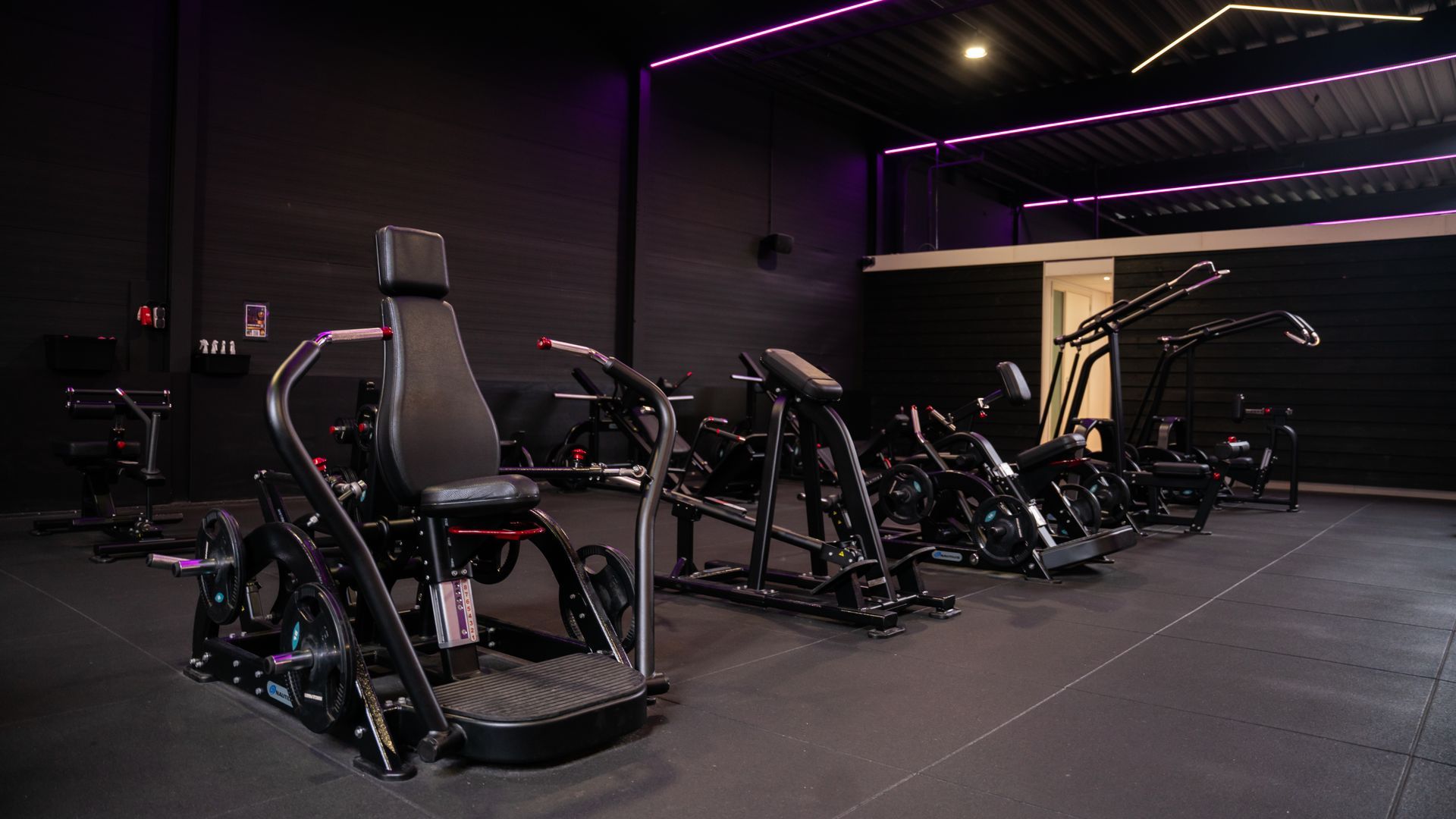 Een rij zwarte fitnessapparaten in een sportschool met paarse accentverlichting.