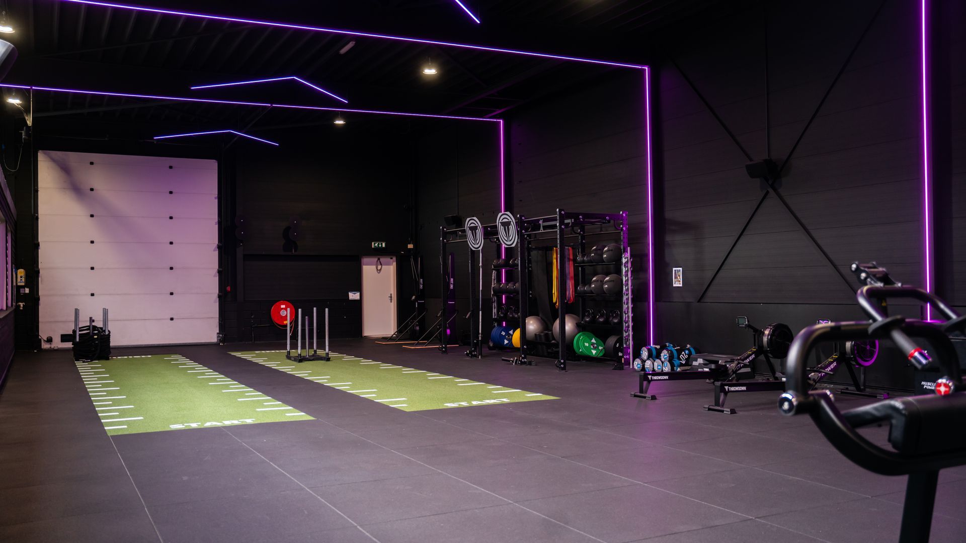 Interieur van een moderne sportschool met fitnessapparatuur en paarse neonverlichting.