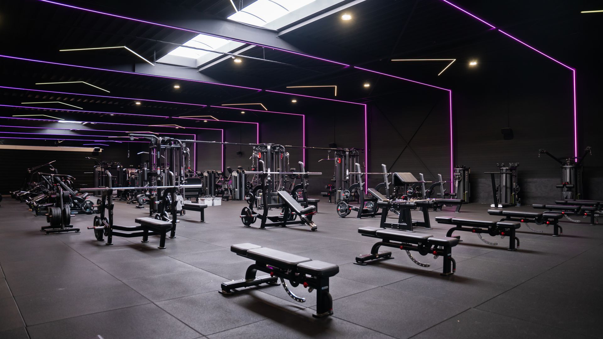 Een donkere, moderne sportschool met fitnessapparatuur. Paarse neonverlichting, donkere vloeren en muren.