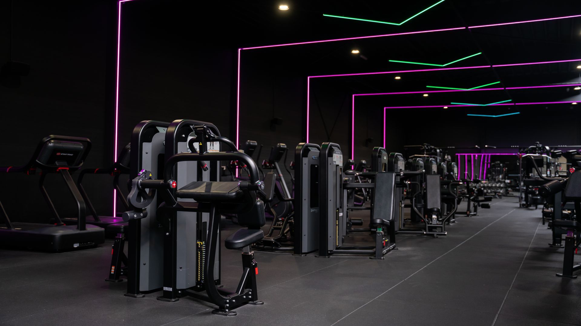 Interieur van een sportschool met fitnessapparaten, zwarte muren en neonverlichting.