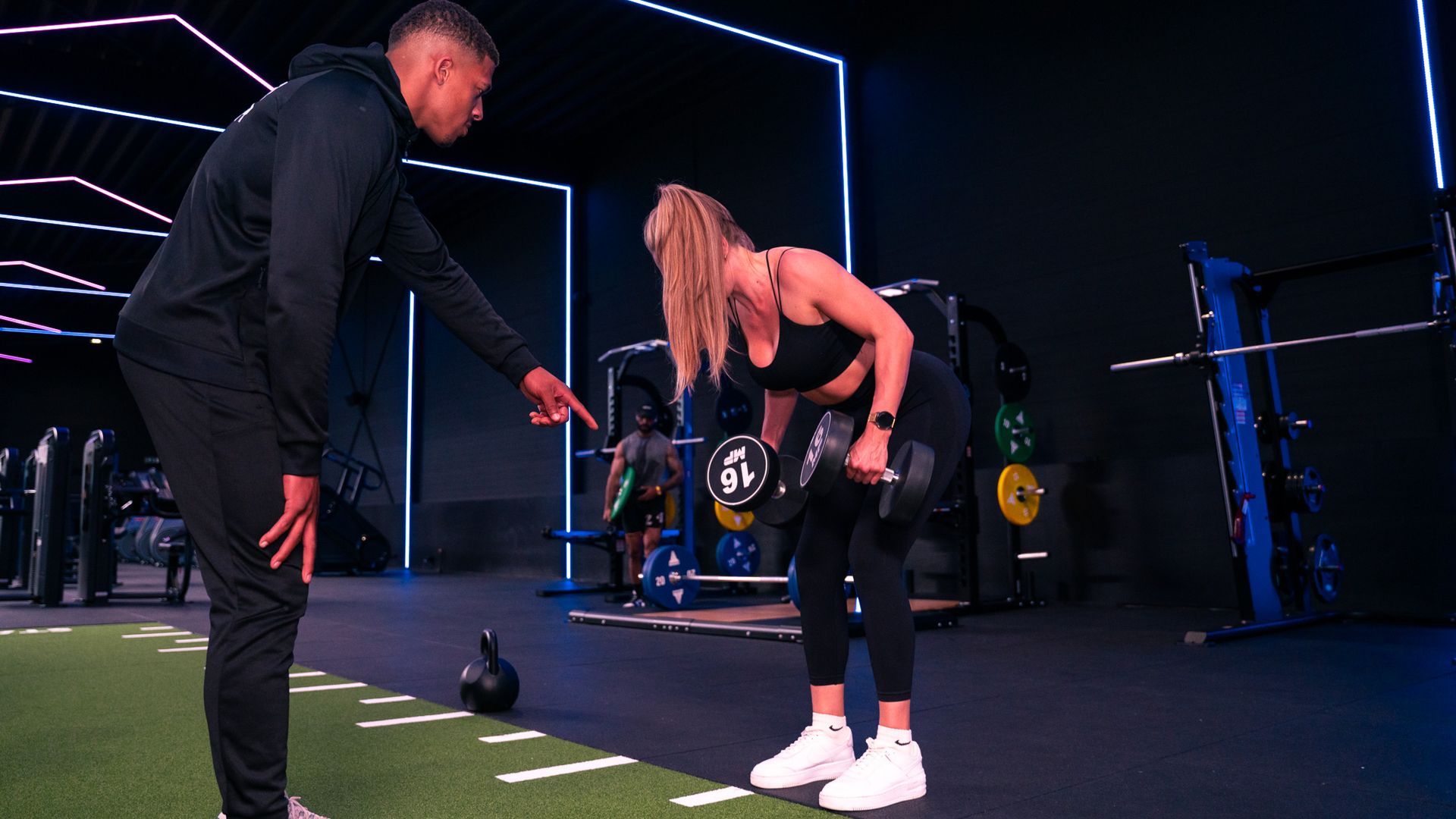 Een trainer helpt een vrouw met dumbbell rows in een sportschool door te wijzen.