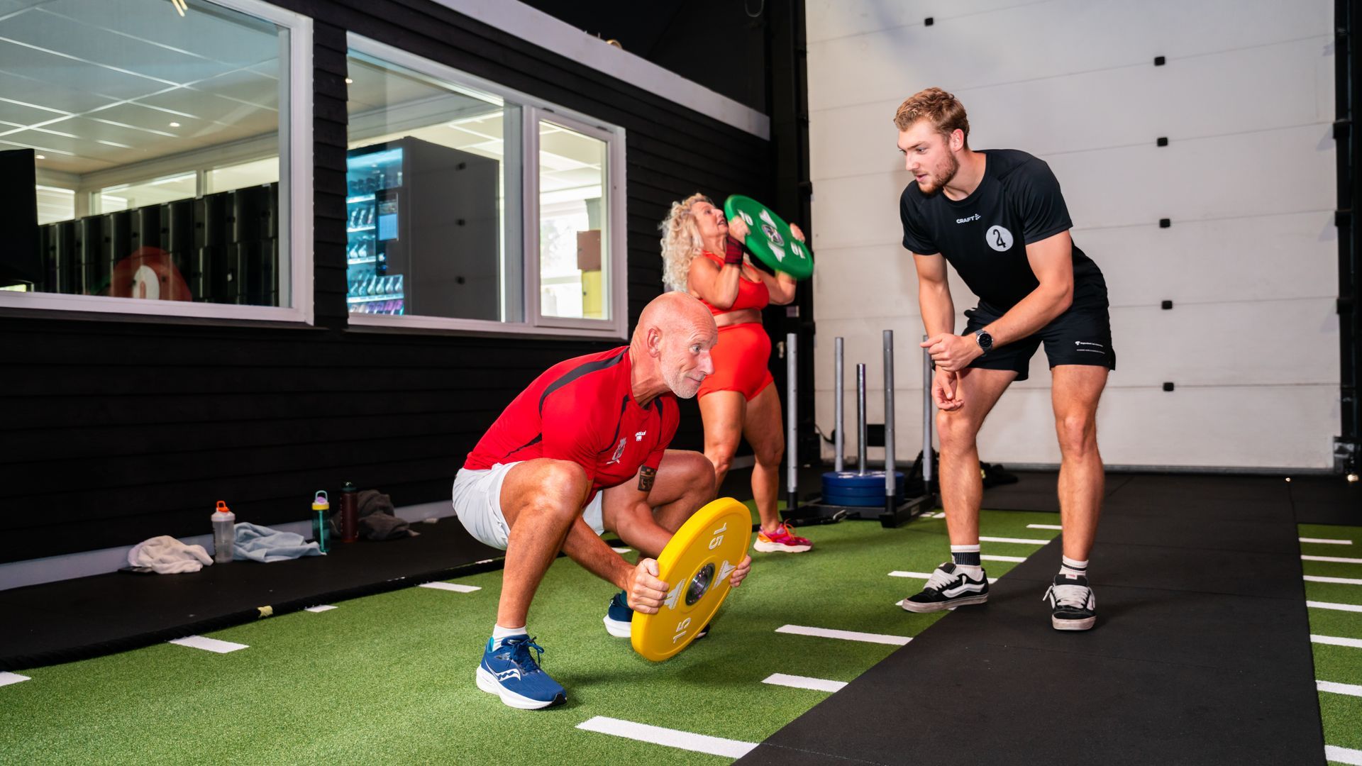 Mensen die onder begeleiding van een trainer in een sportschool met gewichten trainen.