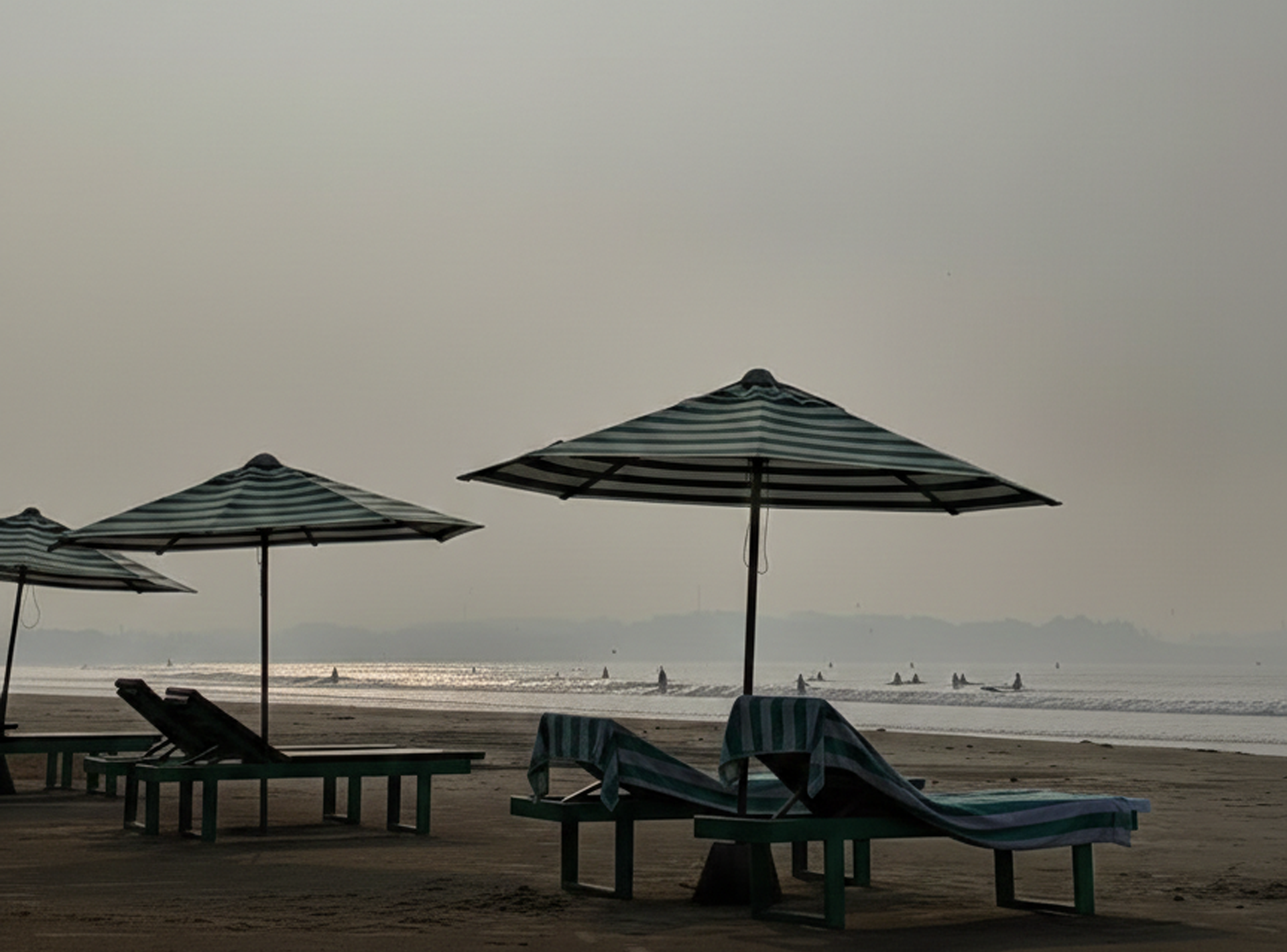 Empty beach with lounge chairs and striped umbrellas under a cloudy sky