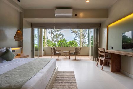 Modern hotel room with king bed, desk, and balcony dining area overlooking lush greenery